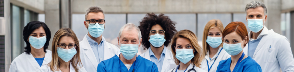 A diverse group of healthcare professionals wearing lab coats and protective face masks, standing confidently in a hospital setting.