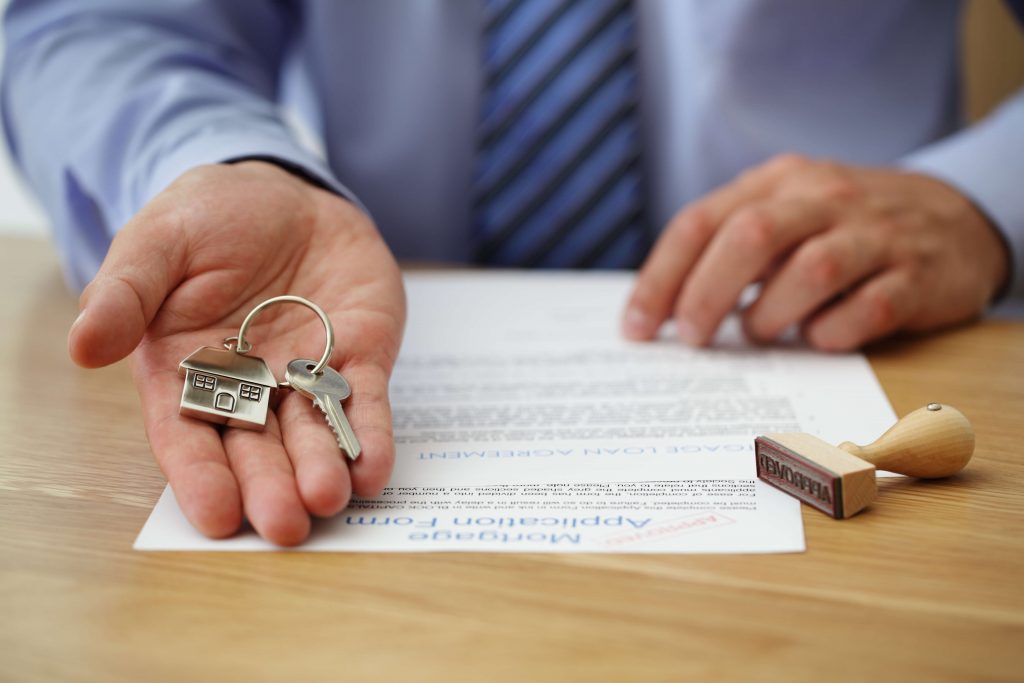 Real estate agent offering house keys over a signed mortgage contract, symbolizing finalizing a house sale