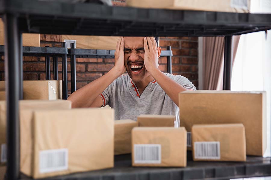  Frustrated man in warehouse with hands on head amid cardboard boxes