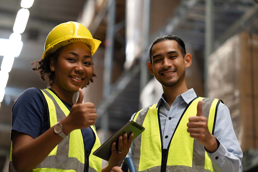 Two warehouse workers in safety gear giving a thumbs-up, signaling efficient operations and teamwork.