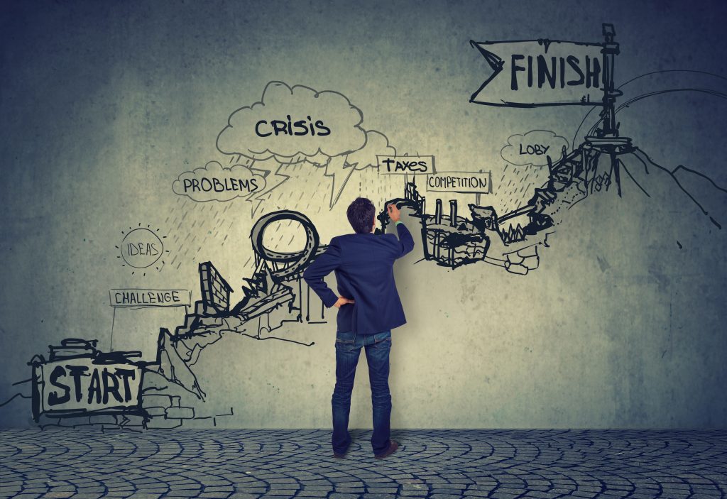 A man in a business suit is examining a complex wall drawing that outlines a challenging journey from 'START' to 'FINISH', with hurdles like 'CRISIS', 'TAXES', and 'COMPETITION' illustrated as part of an obstacle course.