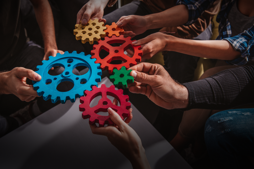 Several hands coming together, holding colorful gear pieces, symbolizing teamwork and integration